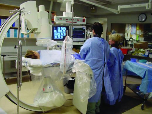 Cardiac catheterization laboratory setup showing fluoroscopy equipment, patient table, and operator positioning